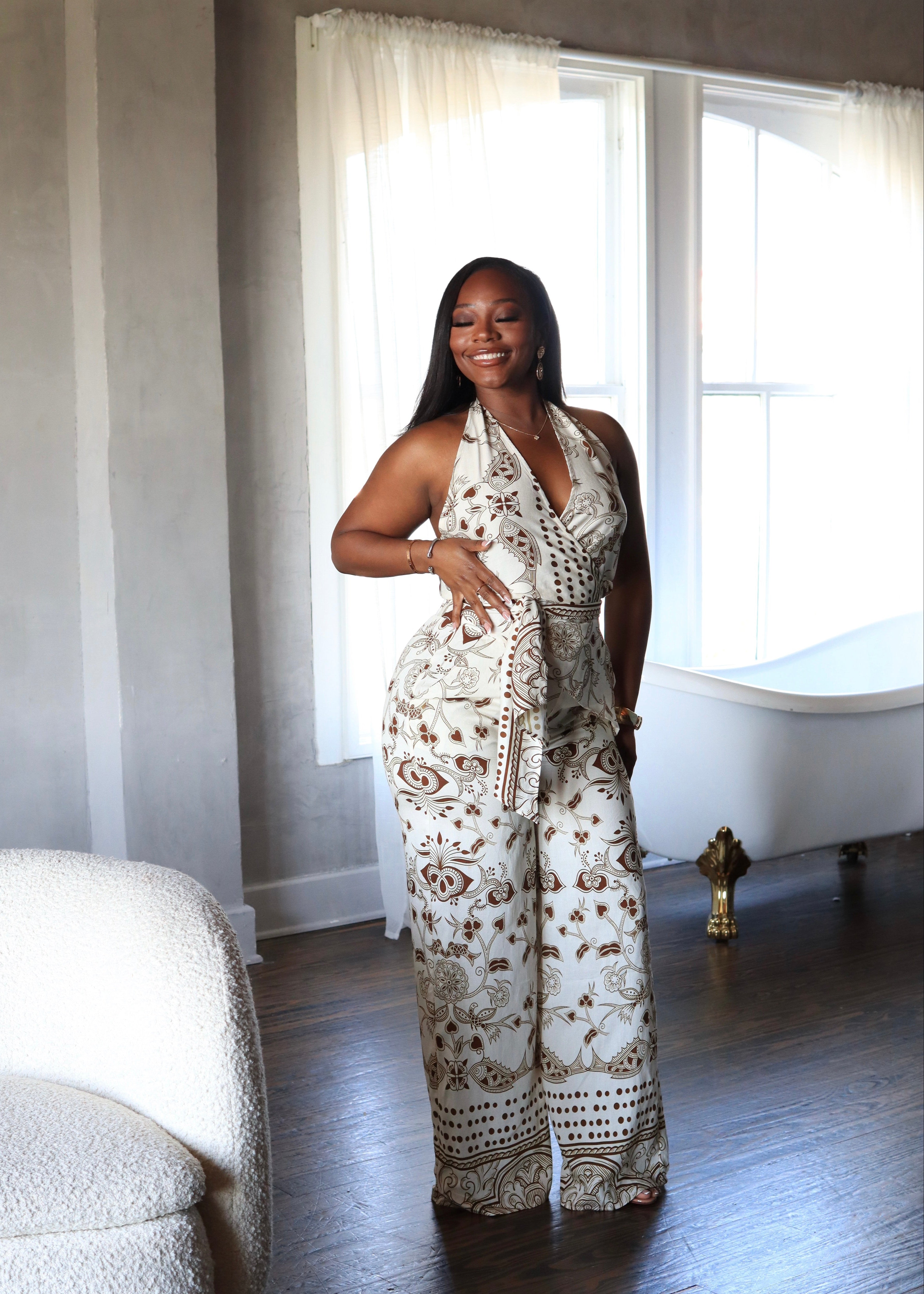 Woman in a patterned outfit standing in a room with a window and chair.