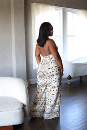 Woman in a patterned dress standing in a room with a white couch and large windows.